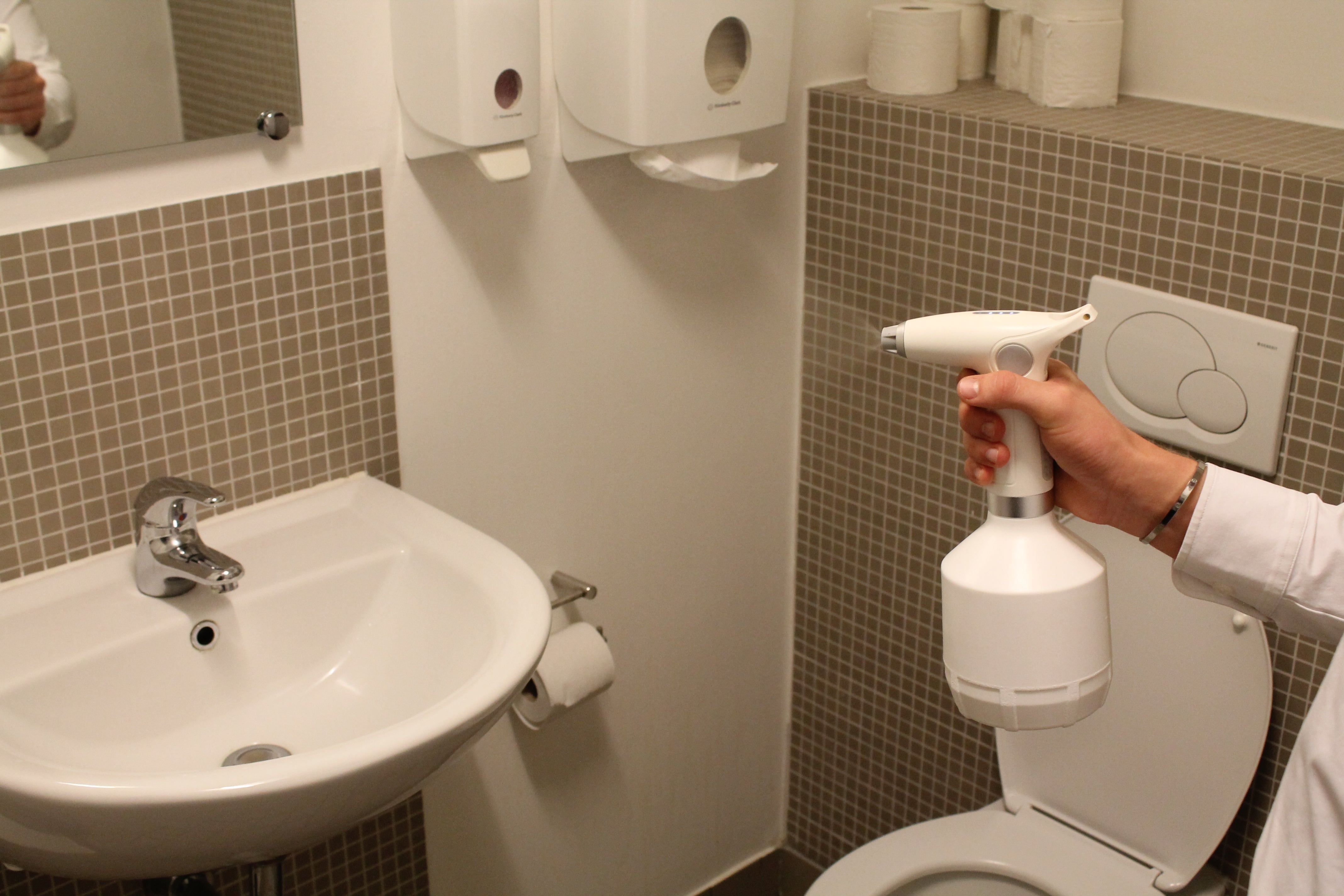 Billeder af safesprayer adjust elektrisk forstøver, som anvendes på et toilet. På billedet kan man se at der kommer væske ud af dysen som har kurs mod vandhanen.